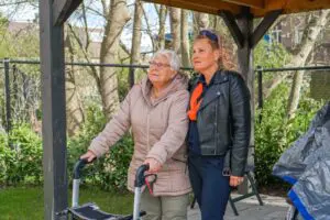 Een bewoonster van het Abtswoudehuis staat samen met haar dochter in de tuin. Ze lijken naar een vogeltje te kijken. 