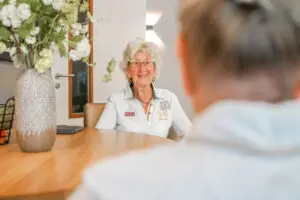 Bewoonster kijkt lachend in de camera terwijl ze samen met haar nichtje aan tafel zit in de huiskamer van Het Zevenheuvelenhuis in Groesbeek, woonzorglocatie voor mensen met dementie.