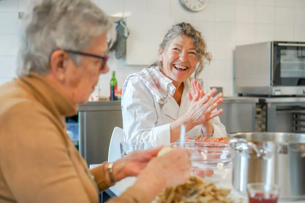 De kok van de kleinschalige woonzorglocatie voor mensen met dementie draait gehaktballen terwijl een bewoonster met alzheimer de aardappels schilt