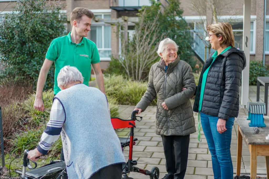 Twee bewoonsters, een met alzheimer en eentje met vasculaire dementie lopen samen met twee zorgmedewerkers een rondje om de zorglocatie voor mensen met dementie van Dagelijks Leven