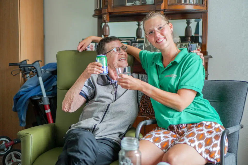 Een bewoonster met Alzheimer proost met een zorgmedewerker in het verzorgingshuis voor mensen met dementie van Dagelijks Leven