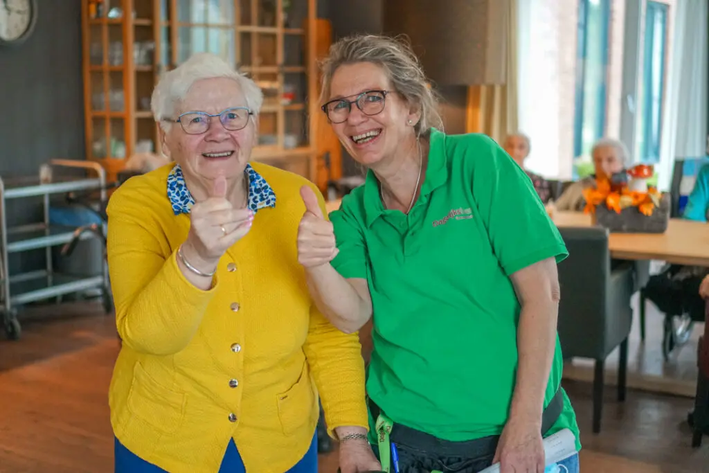 Een bewoonster met Alzheimer en een verzorgende ig steken hun duim om naar de camera in een zorglocatie voor mensen met dementie van Dagelijks Leven