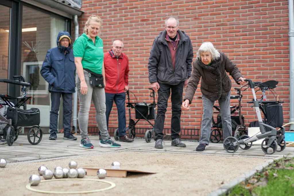 Bewoners van de woonzorglocatie van Dagelijks Leven voor mensen met dementie spelen met elkaar jeu de boules op de jeu de boules-baan die bij de locatie ligt