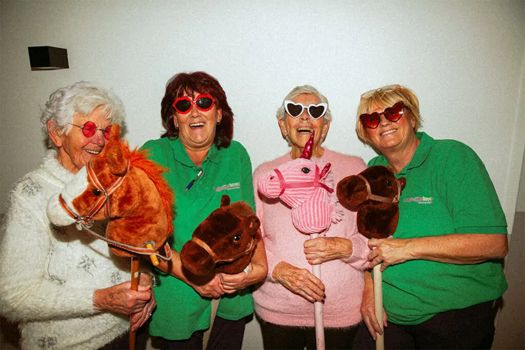 Twee medewerkers van Dagelijks Leven poseren voor lekker met de meiden samen met twee bewoners met dementie. De medewerkers zijn verpleegkundige, verzorgende ig of helpende