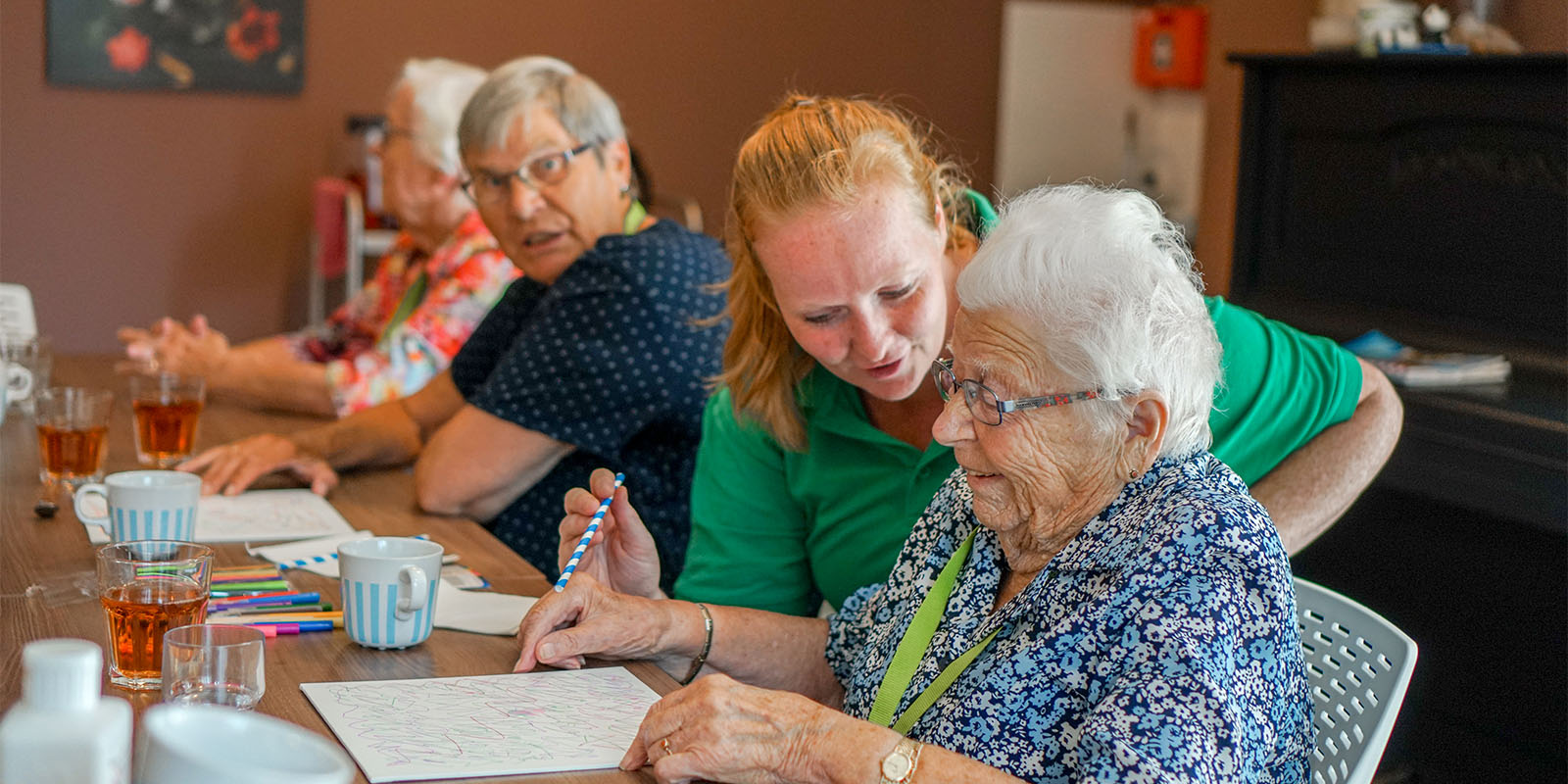 Een bewoner met dementie wordt ondersteund om iets te tekenen of te schrijven op papier.