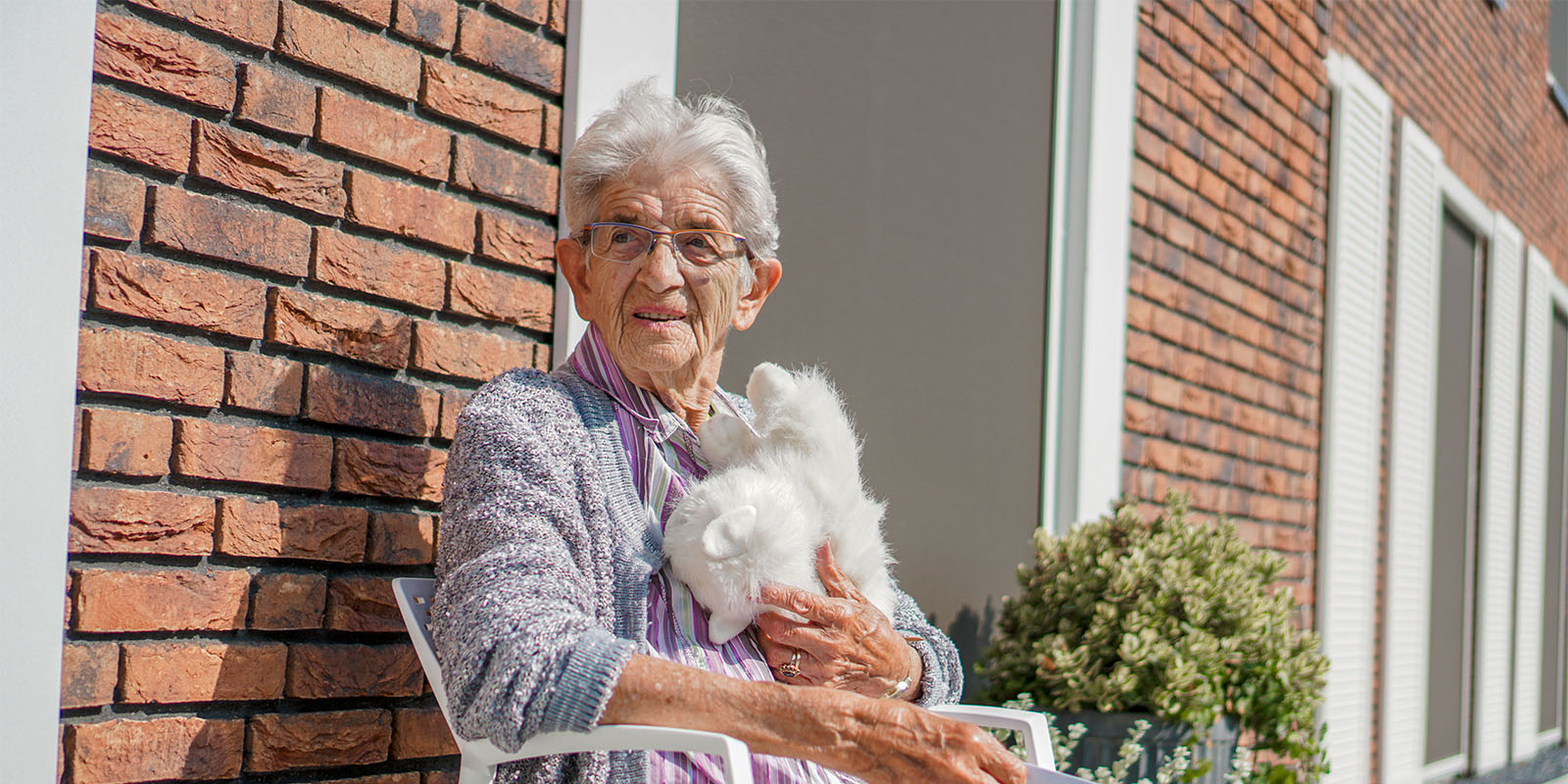 Een mevrouw met dementie zit buiten met een knuffel en kijkt in de verte