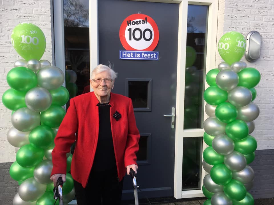 Feest in Het Hurkhuis een bewoonster is 100 jaar geworden en poseert voor de deur met ballonnen