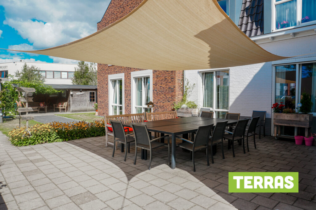 In de tuin van Het Stoofhuis hangt een groot schaduwdoek waar een heerlijk terras is gecreëerd voor de bewoners