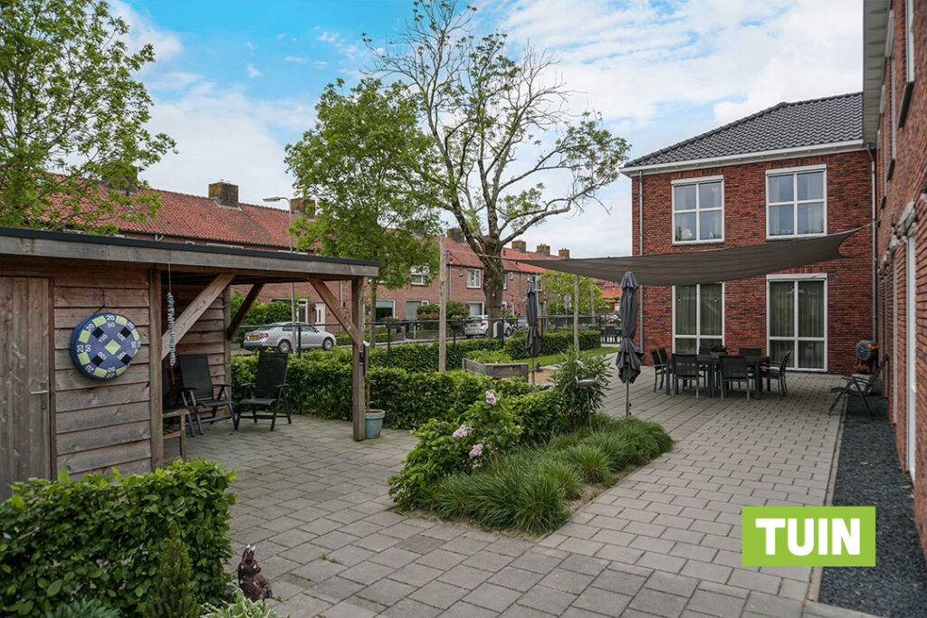 De tuin van Het Vlisthuis, met schuurtje en schaduwdoek bij het terras voor de bewoners met dementie