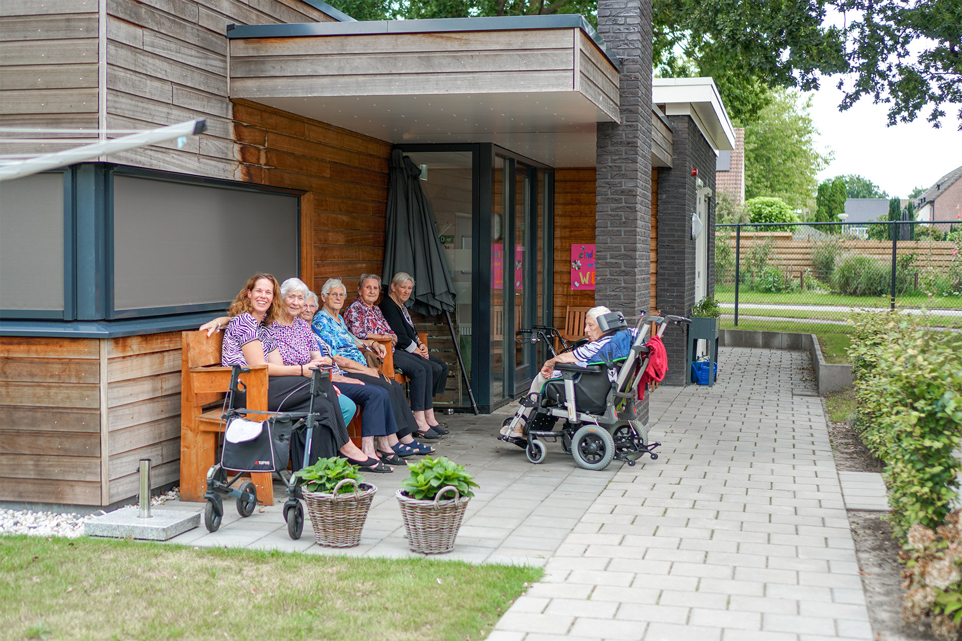 Bewoners zitten gezellig met z'n allen op het bankje in de tuin van Het Rietveldhuis in Emmen