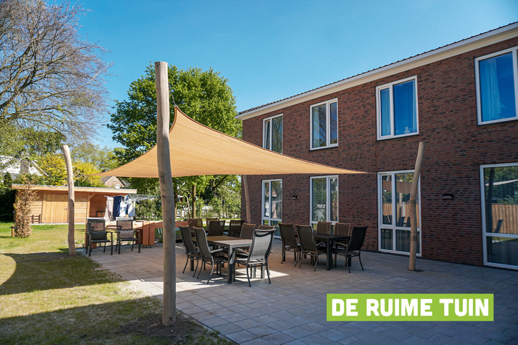 Bewoners wandelen zelfstandig door de open poort naar de tuin in de veilige, dementievriendelijke omgeving van Het Kraatshuis in Ede.