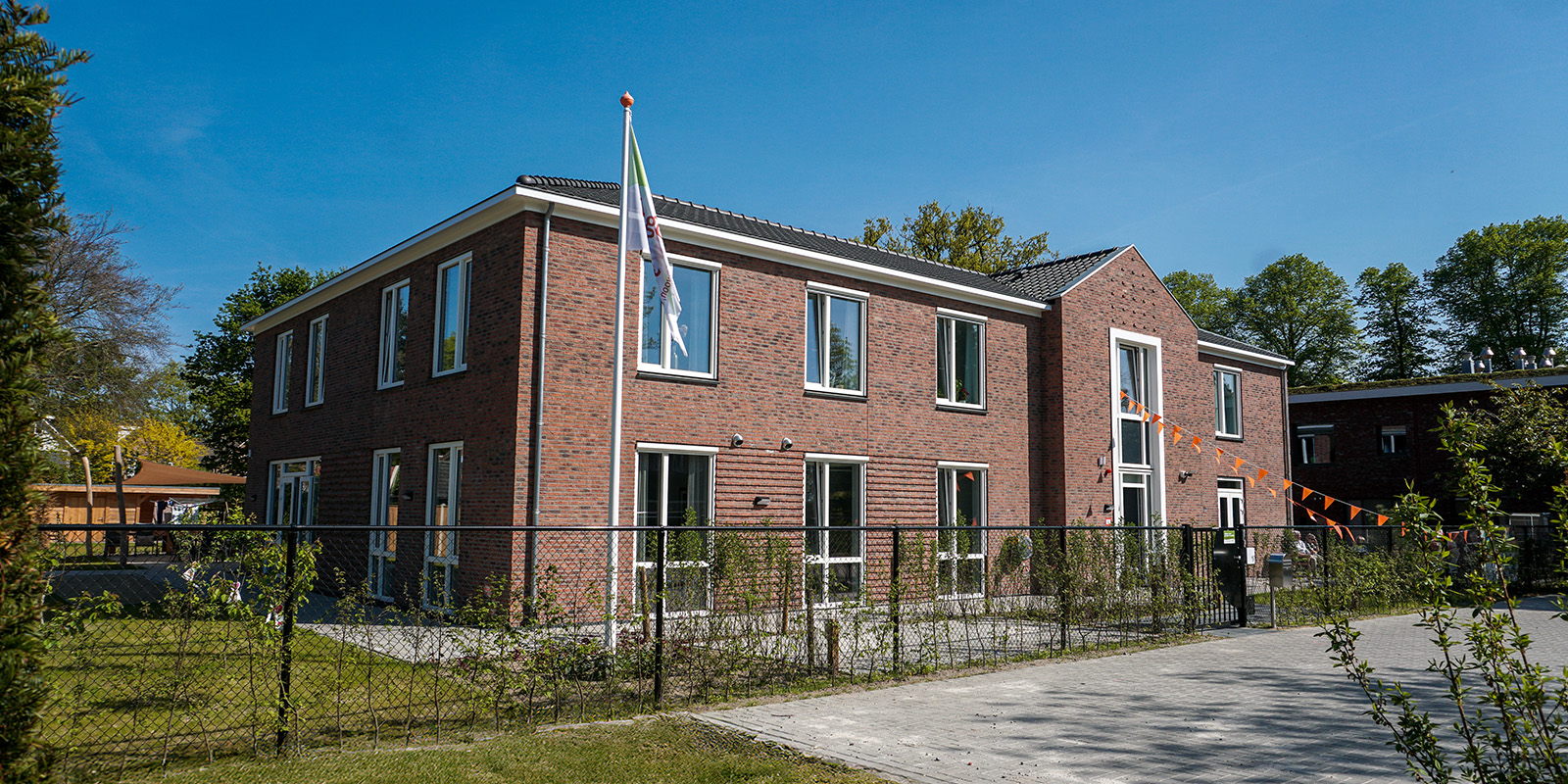 Bewoners wandelen zelfstandig door de open poort naar de tuin in de veilige, dementievriendelijke omgeving van Het Kraatshuis in Ede.
