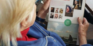 Bewoner van het Biesemhuis in Doesburg leest het magazine van Topstukken on Tour, waarin foto's staan van de bewoners die beroemde kunstwerken nabootsten