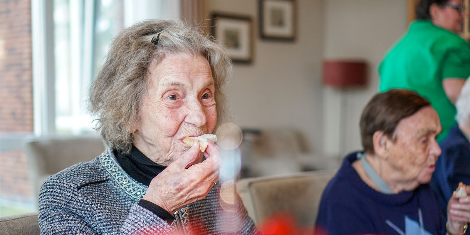 Bewoonster met dementie Dagelijks Leven eet met smaak een boterham aan de gezamenlijke eettafel