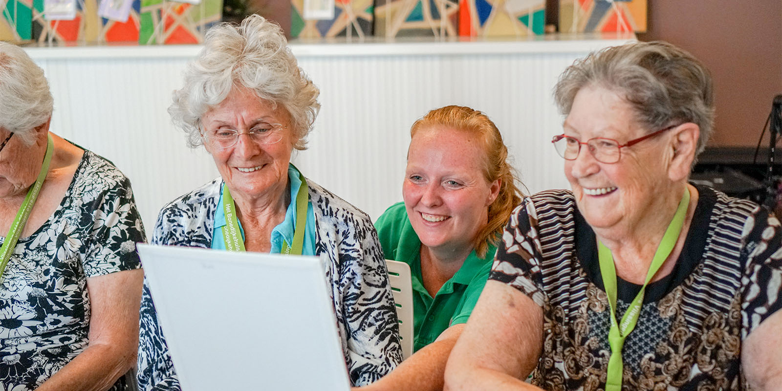 Een medewerkster van Dagelijks Leven kijkt met twee bewoonsters met dementie naar het scherm van de laptop