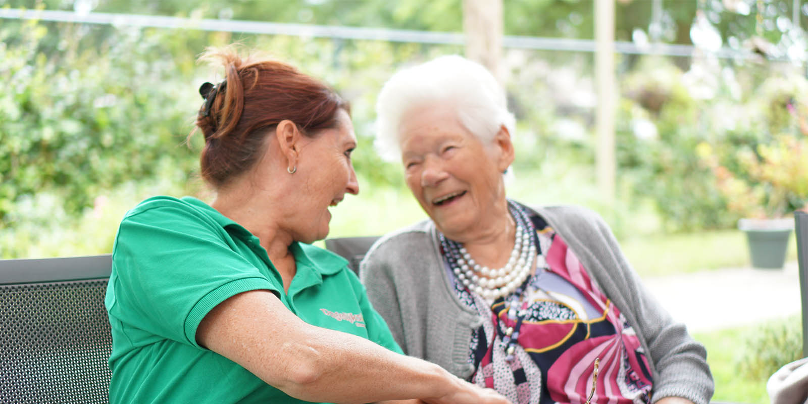 Een verpleegkundige en een bewoner met dementie lachen naar elkaar in de tuin van een kleinschalige woonzorglocatie in Venray.