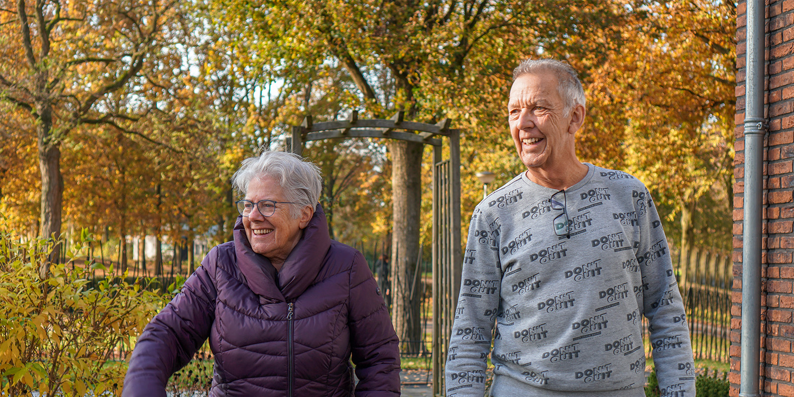 Vrijwilliger wandelt samen met een bewoner door de tuin van een woonzorglocatie van Dagelijks Leven, voor mensen met dementie.