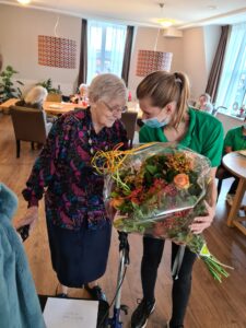 Deze bewoonster van Het Hurkhuis is met haar 102 jaar de oudste inwoner van Helmond. Ze krijgt het boeket van de burgemeester overhandigd door een zorgmedewerker van Dagelijks Leven.