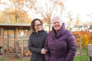 Bewoner van Dagelijks Leven wandelt door de tuin van een kleinschalige woonvorm voor mensen met dementie, samen met haar dochter. 