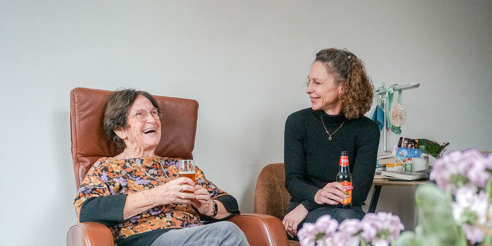 Een bewoner met dementie drinkt samen met haar dochter een biertje in haar studio in Het Greidenhuis in het Friese Heerenveen. Ze moeten hard lachen.