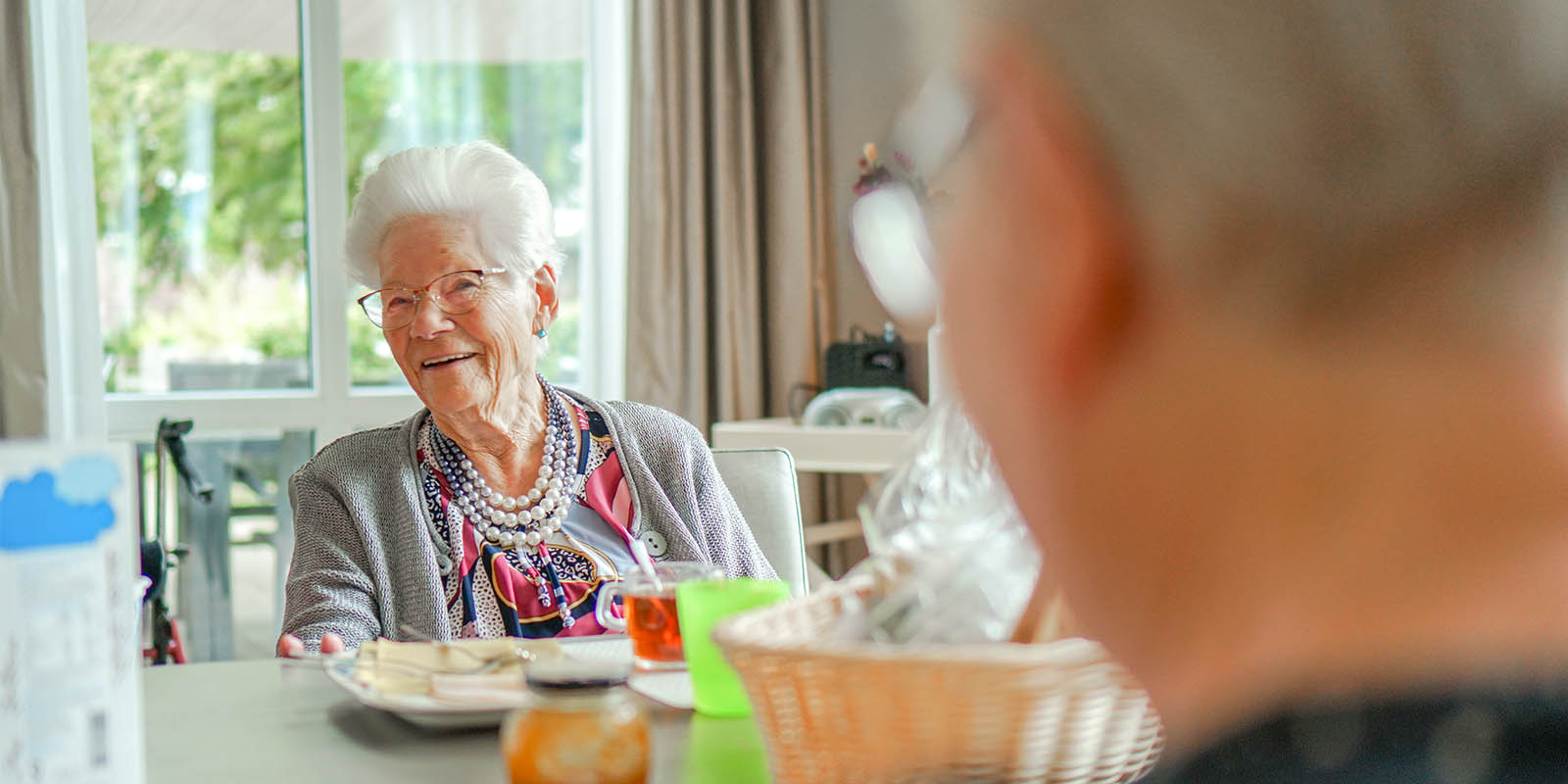 Een bewoner lachend aan tafel in een woonzorglocatie voor mensen met dementie, van Dagelijks Leven. Ter illustratie bij een blog over het werk van een gastvrouw.