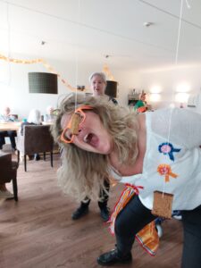Geesje doet tijdens Koningsdag in Het Rietveldhuis even voor hoe het nou precies moet, koekhappen. Ze werkt als activiteitenbegeleider op de kleinschalige woonzorglocatie voor mensen met dementie in Emmen. 
