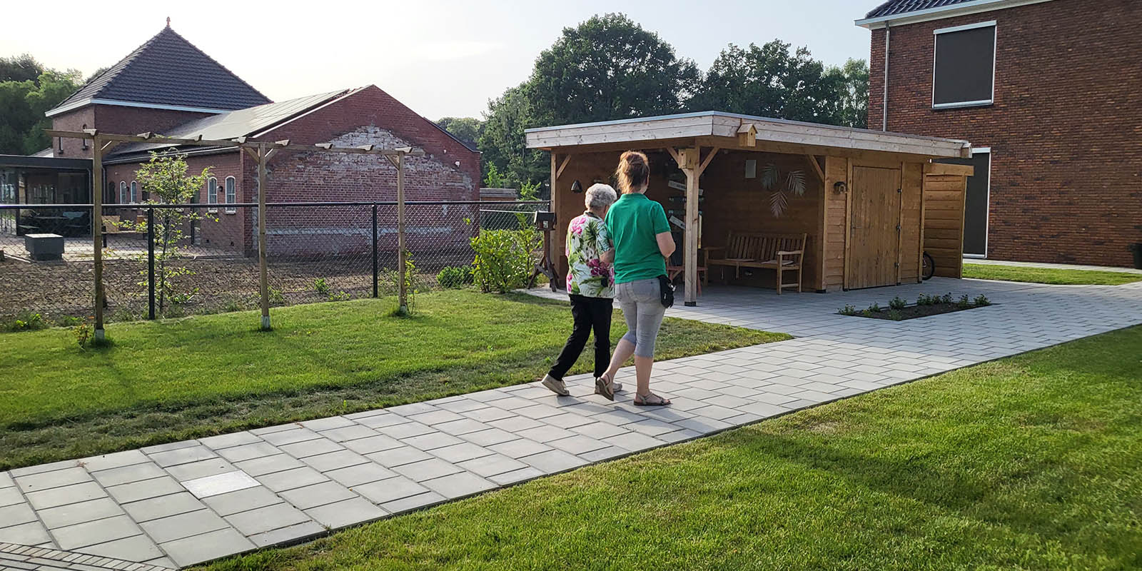 Een GVP wandelt samen met de bewoonster door de tuin van een woonzorglocatie van Dagelijks Leven, voor mensen met dementie. De foto hoort bij de blog over verdriet en eenzaamheid bij dementie.