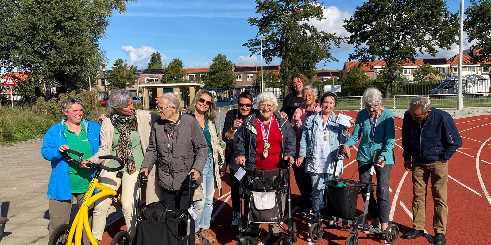 Bewoners van Het Houwinghuis, woonzorglocatie voor mensen met dementie, op de atletiekbaan in Den Helder na afloop van de Helderse Rollatorloop. Ze laten trots hun medailles zien.