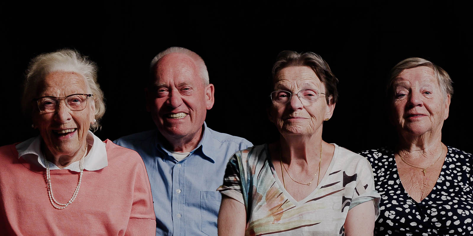 Vier bewoners op rij, voor een zwarte achtergrond. Ze lachen allemaal in de camera. Beeld uit de campagne: werken in de dementiezorg: weet waar je het voor doet.