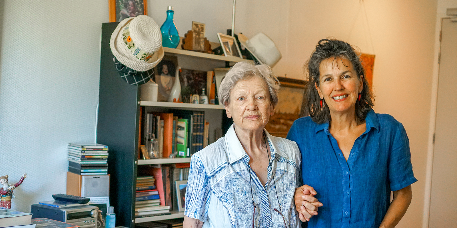 Bewoonster met dementie samen met haar dochter in haar studio in het huis van Dagelijks Leven. Ze staan voor de bomvolle boekenkast. Mevrouw leest graag.