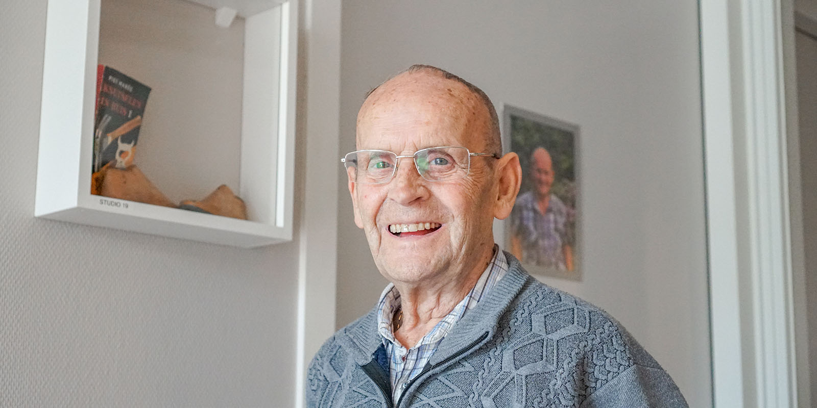 Portretfoto van Gerrit, voor zijn studio in Het Zevenheuvelenhuis in Groesbeek, waar hij vanwege zijn dementie woont. Hij lacht in de camera.