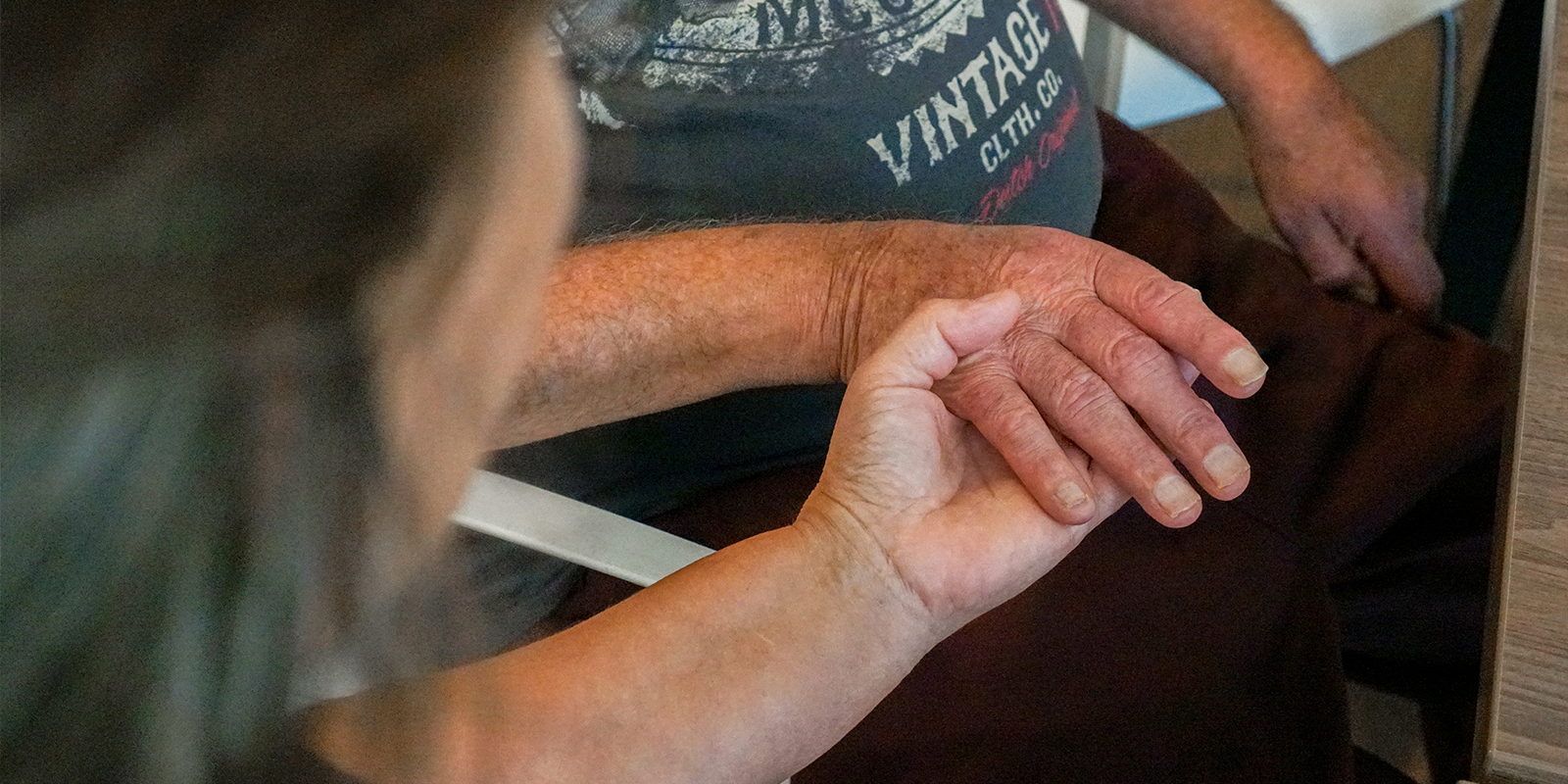 Foto van een verzorgende die een hand van een bewoner met dementie vasthoudt. Voor bij een blog over het werk van een stervensbegeleider.
