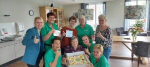 Het Braassemhuis, woonzorglocatie voor mensen met dementie in Roelofarendsveen, is uitgeroepen tot Zorgtopper 2023 in de gemeente Kaag en Braassem. Op de foto collega's met een bewoner, de taart en het tegeltje. 