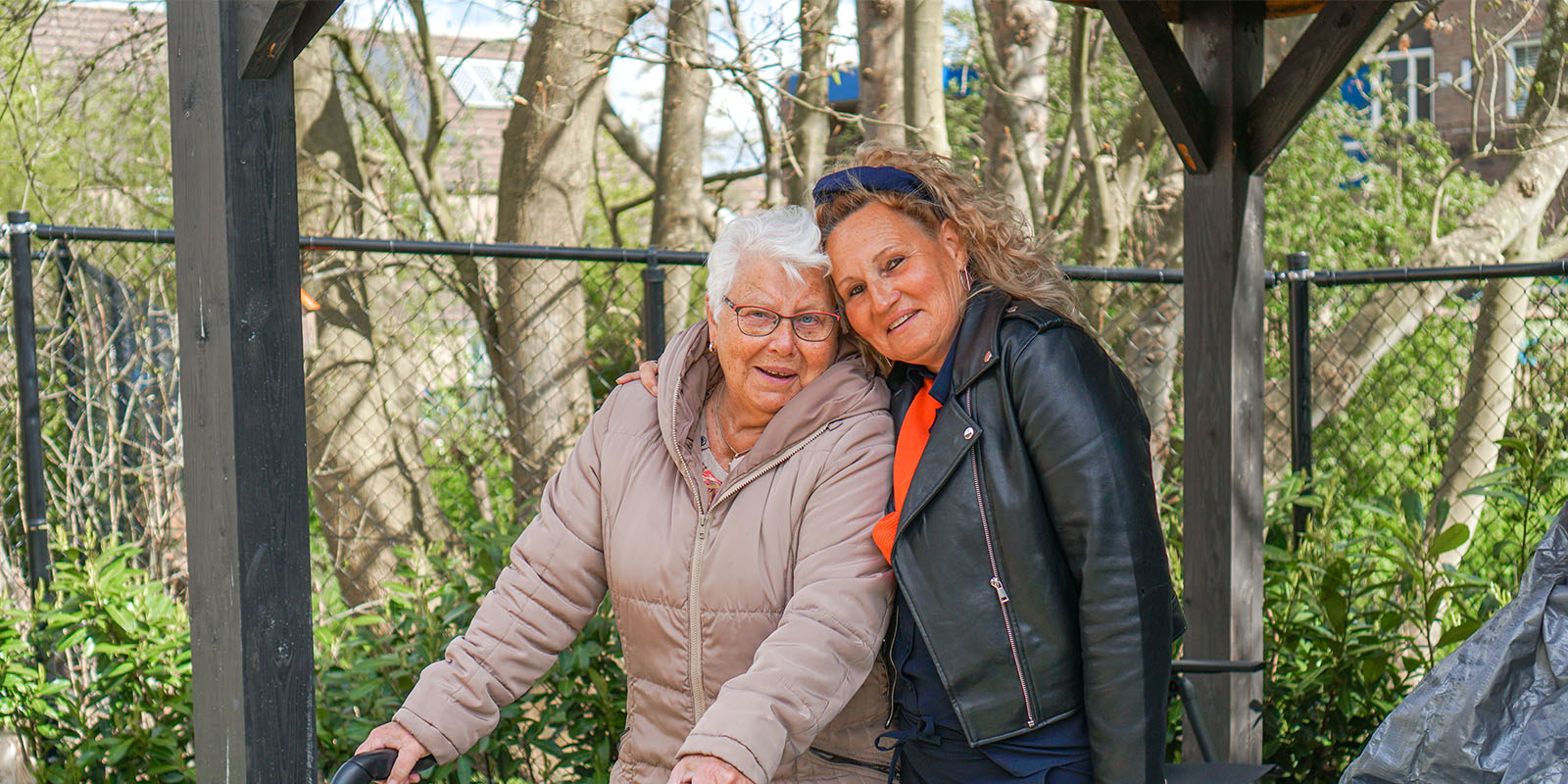 Moeder en dochter samen aan de wandel in de tuin van de kleinschalige woonzorglocatie voor mensen met dementie van Dagelijks Leven.
