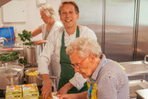 Kok van Dagelijks Leven samen met bewoners aan het koken in de keuken van een woonzorglocatie voor mensen met dementie.
