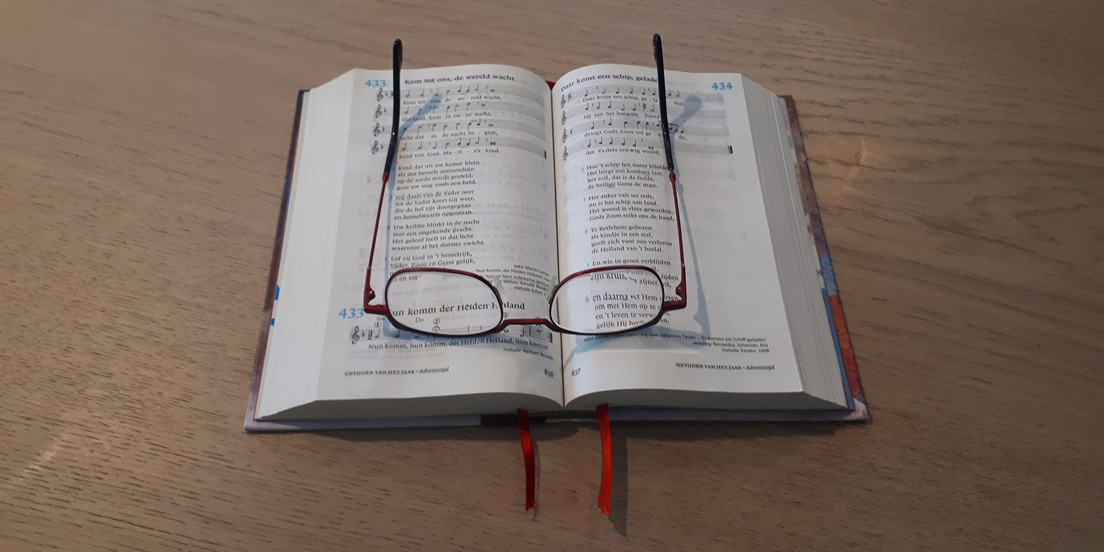 Foto van een liedboek met psalmen met daarbovenop de bril van de bewoonster met dementie.