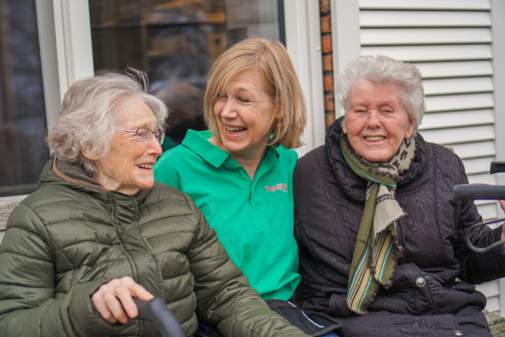 Een bewoonster met Alzheimer, een verpleegkundige en een bewoonster met vasculaire dementie zitten buiten op een bankje voor het verpleeghuis van Dagelijks Leven
