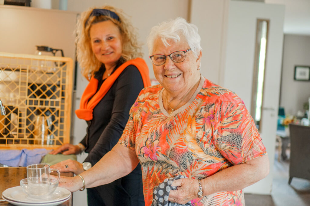 Een vrijwilligster en een bewoonster met Alzheimer doen samen de afwas in het verzorgingshuis van Dagelijks Leven