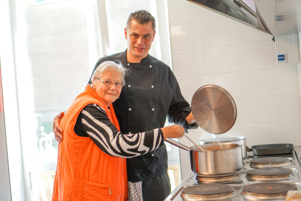 Een bewoonster met Alzheimer helpt de kok met het koken van de soep voor het eten in de kleinschalige woonzorglocatie voor mensen met dementie
