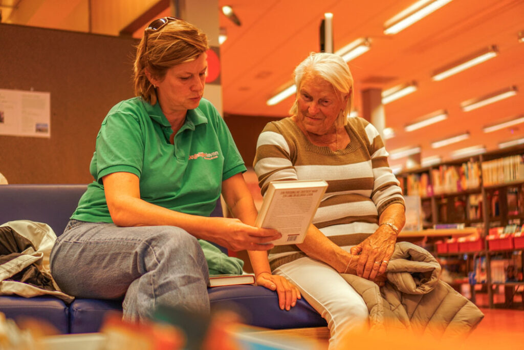 Een bewoonster en medewerker van de kleinschalige woonzorglocatie voor mensen met dementie zijn samen naar de bibliotheek en lezen een boek