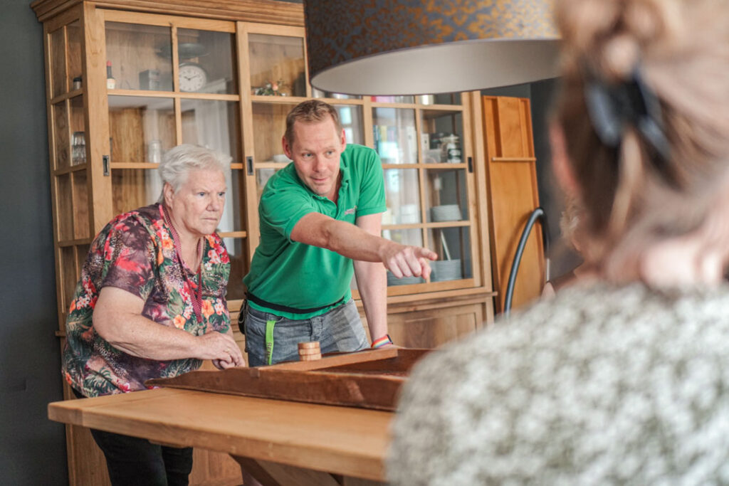 Een bewoonster met dementie en de verzorgende spelen samen een potje sjoelen op de woonzorglocatie van Dagelijks Leven